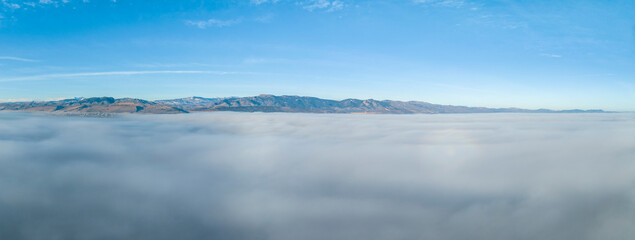 dense fog covering foothills of northern Colorado with cler mountains at a horizon, aerial view of winter morning