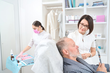 Experienced cosmetologist advises an elderly man,man holds a mirror