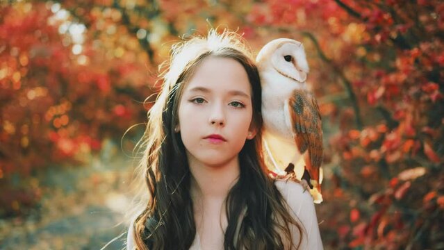 Fantasy portrait girl princess teenager enjoys nature with white bird barn owl on shoulder. Beauty face looking at camera enjoying nature, divine sun light. Autumn nature forest trees. vintage dress