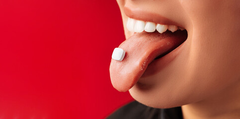 Close up shot of a female tongue holding a square shaped pill or sweet drop.