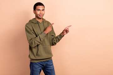 Photo of student guy young man wear khaki sportswear hoodie direct fingers mockup opening new shop advert isolated on beige color background