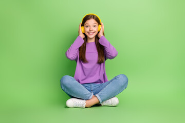 Full size photo of good mood girl with long hairdo dressed denim jeans palms touching headphones isolated on green color background