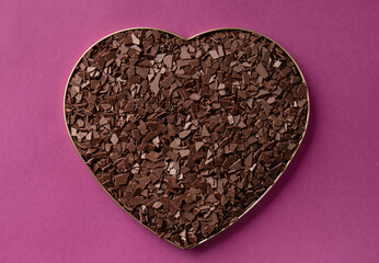 Dark chocolate in the shape of a heart on a purple background top view.