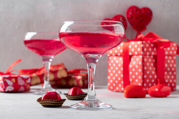Two glasses of shimmering pink champagne and heart-shaped candies on gray background. Romantic dinner for a couple