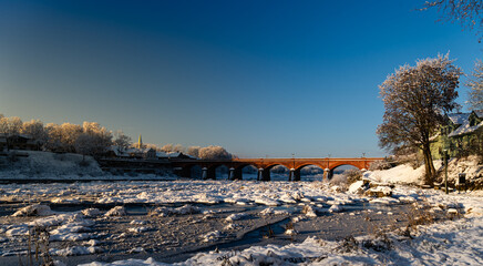 Winter view of an old brick bridge over a frozen river on a sunny day
