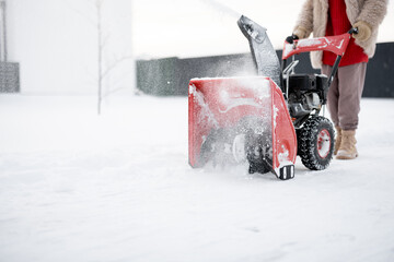 Person pushing a snow thrower machine, cleaning a pathway from the snow, close-up on machine that blows snow away