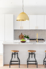 A kitchen detail with white cabinets, gold faucet and light hanging over the island with bar...