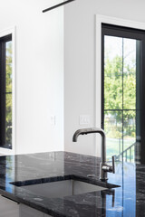 A modern kitchen black stainless faucet detail on an island with a black marble countertop, black...