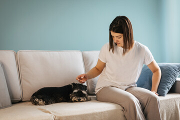 Beautiful caucasian woman takes a selfie near her little black dog miniature schnauzer breed sitting on the couch at home