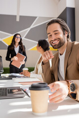 smiling manager reaching takeaway drink while interracial businesswomen talking on blurred background.