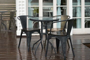 Wet tables with chairs outside the restaurant in the rain. There are puddles on the wooden floor.
