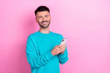 Photo of positive man toothy smile hold use telephone empty space isolated on pink color background