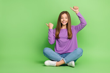 Full size photo of optimistic cute girl with long hairstyle dressed jeans directing empty space isolated on green color background