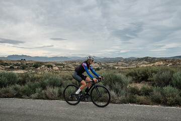 Naklejka na ściany i meble woman cyclist riding a gravel bike with a view of the mountains, Murcia region of Spain
