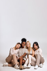 Portrait of diverse group of models sitting on floor, young females in basic clothing look at camera, having rest, friendly women have different race and skin, hair colour. natural beauty concept