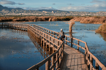 a female cyclist rides a bicycle on a wooden bridge over a river