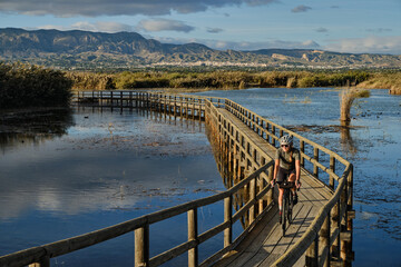 a female cyclist rides a bicycle on a wooden bridge over a river