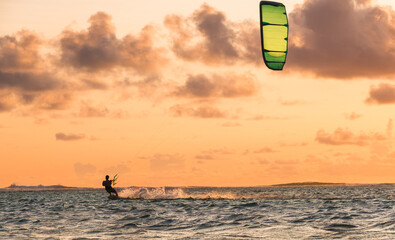 Sunset sky over the Indian Ocean bay with a kiteboarder riding kiteboard with a green bright power kite. Active sport people and beauty in Nature concept image. Le Morne beach, Mauritius.