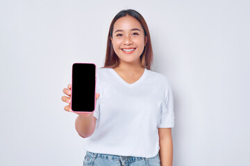 Fototapeta premium Beautiful smiling Asian girl wearing casual white t-shirt showing smartphone with blank screen isolated on white background. People lifestyle concept