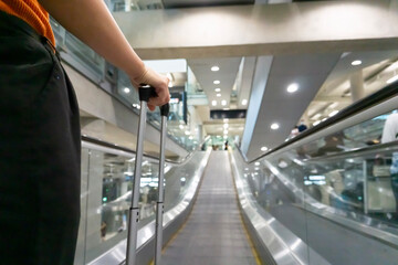 Traveller female holding suitcase on escalator at airport or transit flight with luggage on holiday traveling in elevator arriving at international airport.