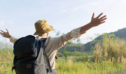 Happy male mountain hiker standing and looking at mountains with arms outstretched towards valley with blue sky. Happy man enjoying nature on the mountain and raising his hands to the sky.