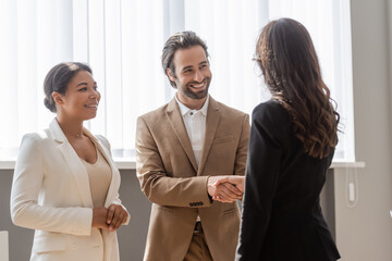 happy man shaking hands with business partner near smiling multiracial colleague.