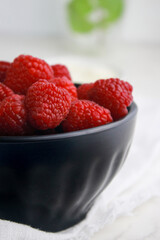 close up of fresh raspberries in dark bowl, blurred white background 