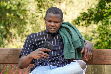 portrait of black man from africa looking at mobile in a park