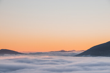 View of sea of clouds colored in the soft orange-pink hue of the morning sun. Peaks of the...
