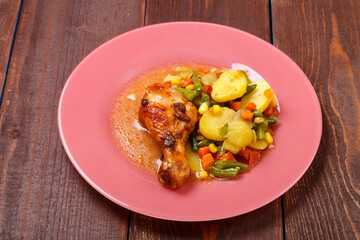Baked chicken drumstick with vegetables in sauce and spices on a wooden table.
