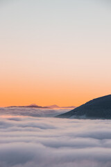 View of sea of clouds colored in the soft orange-pink hue of the morning sun. Peaks of the...
