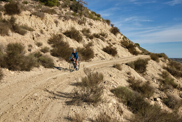 female cyclist riding a gravel bike on a gravel road with a view of the mountains, Alicante region of Spain