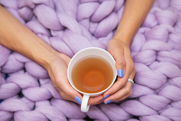 A girl wrapped in a large pink merino wool blanket, a warm and very soft blanket, a girl holding a cup of hot white tea, top view.