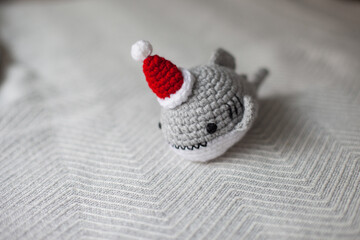 Crocheted plush shark in Santa hat as Christmas gifts. Amigurumi toys handmade. Crochet hobby. Making DIY gifts for family and friends and kids. Natural light background.