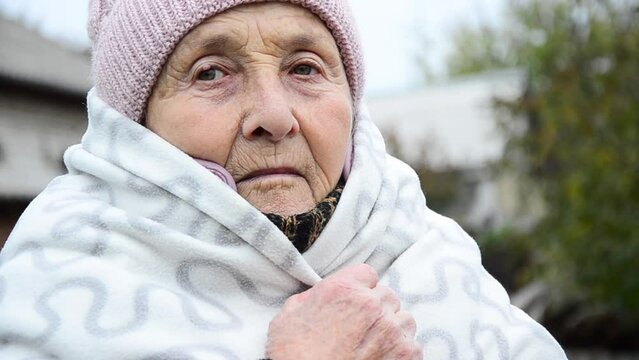 A woman wrapped herself in a blanket during the war. Winter in Ukraine during the war. War in Ukraine. The face of an old woman. Wrinkled face close-up. Sad Ukrainian woman. Stop war. Peace concept