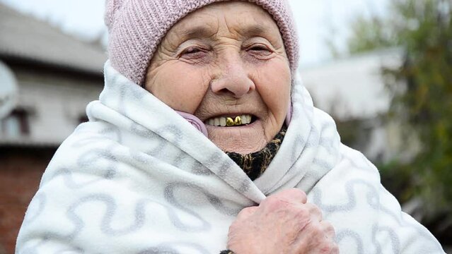 Grandma smiles. Old face close up. Wrinkled face. Grandmother warms herself during the cold. Winter in Ukraine during the war. Shelling of Ukrainian infrastructure. War in Ukraine. Russian aggression 