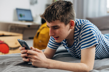 Teenage boy uses his phone on the bed