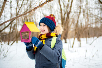 happy boy hangs a bird feeder on a tree. boy activist with a feeder in his hands. day in the park in winter or spring.