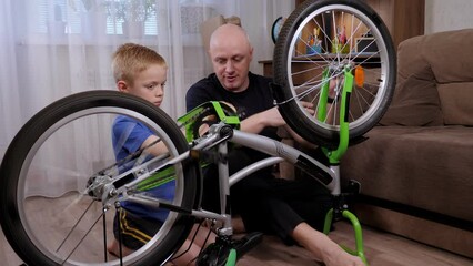 Portrait of a young father and his son repair a broken bicycle together at home. A father teaches his son how to unscrew screws with a wrench.