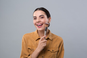 Happy woman with makeup brush on light grey background