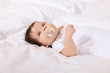 Cute little baby with pacifier lying on bed