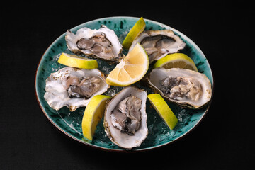 Oysters served with lemon and ice on blue plate on black background