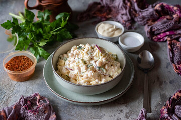 A hearty lunch for the family: a delicious and appetizing salad with vegetables, beans, fresh herbs and mayonnaise in a beautiful green plate on a light background. Close-up