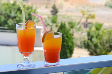 Freshly prepared delicious cocktails with straws and orange slices on the hotel balcony on the background of green plants