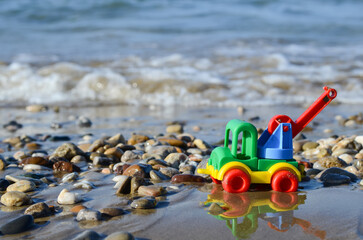 Multi-colored plastic car on the sand against the background of the sea. Kids toys