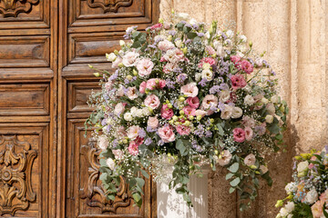 Fototapeta na wymiar Luxury wedding floral decorations at the entrance of Ostuni church. Wedding celebrations in south Italy. Big bouquets of colorful flowers.