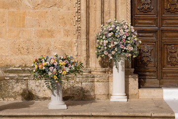 Luxury wedding floral decorations at the entrance of Ostuni church. Wedding celebrations in south Italy. Big bouquets of colorful flowers.