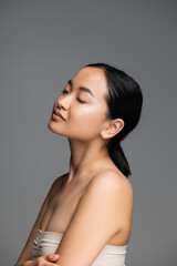 charming asian woman with closed eyes and perfect skin posing isolated on grey.