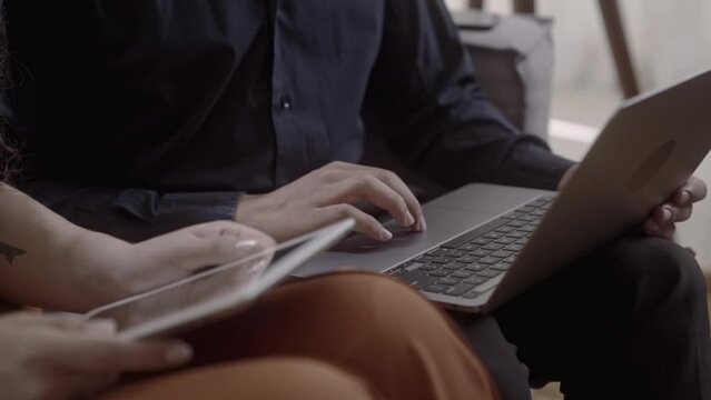 Latin Couple Using A Laptop And Tablet And Talking