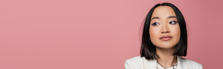 Obraz premium portrait of brunette asian woman with makeup looking away isolated on pink, banner.